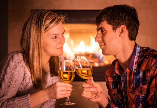 Happy young couple sitting near fireplace and drinking wine