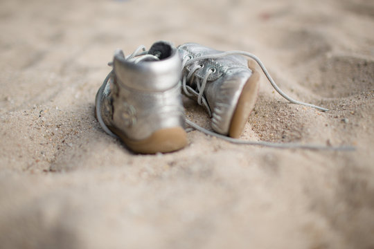 two silver colored kids shoe lie in the sand. 