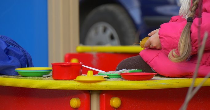 Little Girl Hands Close Up is Playing Cook Toy Plates on a Table with Sand Toy Dishes Toy Food Forks Spoon Girl is Playing in the Sandbox Outdoors Fall