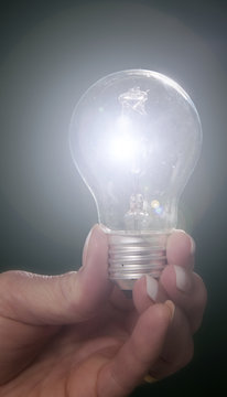 Woman's hand holding an illuminated household lightbulb