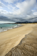 A natural sharp line printed in wet sand along the beach. In the background the ocean, mountains and a cloudy sky