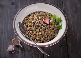 Boiled lentils in a bowl with garlic and black pepper on a wooden table