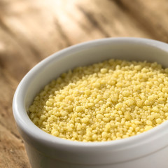 Raw couscous in small bowl on wood photographed with natural light (Selective Focus, Focus one third into the couscous)