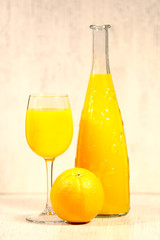 Fresh orange lemonade in a glass next to the whole fruit and orange slices on a light gray background. Selective focus