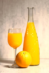 Fresh orange lemonade in a glass next to the whole fruit and orange slices on a light gray background. Selective focus