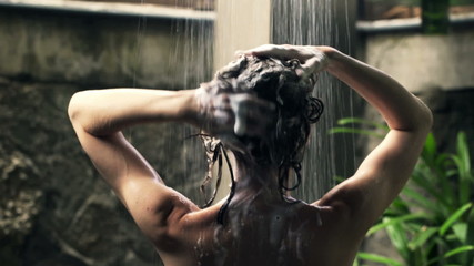 Young woman washing hair under shower in open bathroom 
