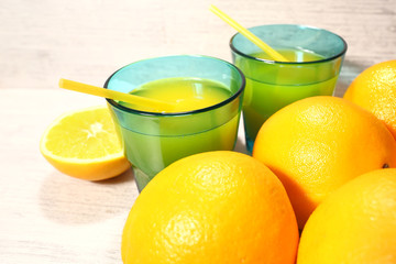 Fresh orange lemonade in a glass next to the whole fruit and orange slices on a light gray background. Selective focus