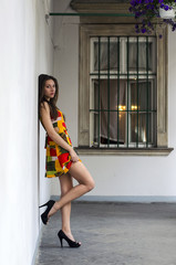 Симпатичная девушка брюнетка в красивом красочным платьем в светлом дворике старого города летом на фоне окна