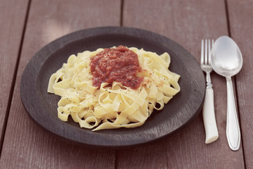 Tagliatelle with tomato sauce in wooden plate, toned