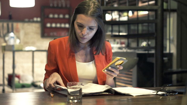 Businesswoman working with smartphone and documents by table at home
