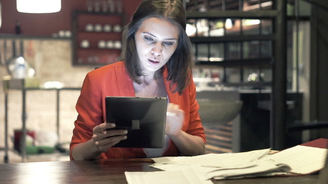 Young businesswoman comparing data on tablet computer and documents by table at kitchen
