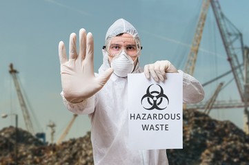 Technician in coverall warns in landfill about hazardous waste.