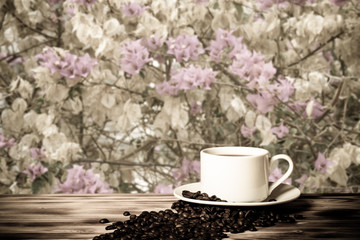 Coffee beans and coffee in white cup on wooden table opposite a