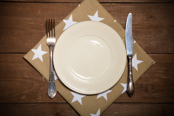 Plate, fork and knife on napkin on wooden background. Toned