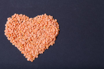 Orange lentils in a heart shape on a black background