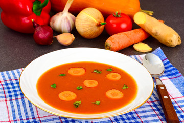 Carrot Tomato Soup in Plate. Behind lie on the soup ingredients,