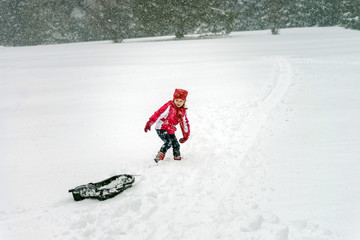 Little girl playing with sled in  snow while snowflurry