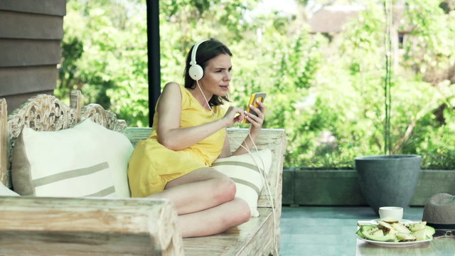 Happy woman listen to music on  smartphone on wooden sofa on terrace

