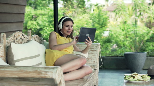 Young, happy woman watching funny movie on tablet on sofa on terrace
