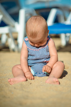 little baby sitting on the sand in a striped jumpsuit
