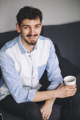 Handsome casual man sitting on couch having coffee 