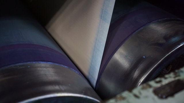 Close up handheld shot of the cyan drums on an industrial offset printing press with the paper between the drums and starting to turn as the process is being set up for a newspaper run.