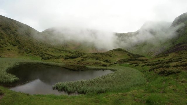 Dense fog covering top of the hills near the the mountain lake panorama from left to right
