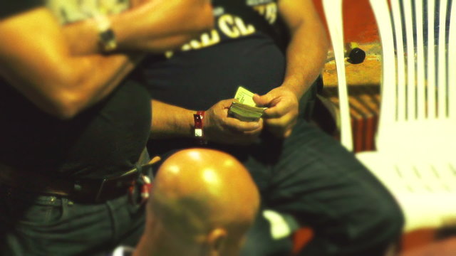High stakes gambler meticulously counting dollar bills while immersed in a thrilling cockfight tournament,showcasing the intensity of the event.