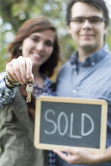 couple holding keys and sold sign excited for their new real estate home purchase or new car