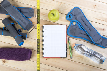 Sport Equipment. Dumbbells,  Ankle Weights, Wrist Weights, Towel, Tape Measure, Bottle Of Water, Notebook To Workout Plan On Wooden Table. Sport Fitness Background