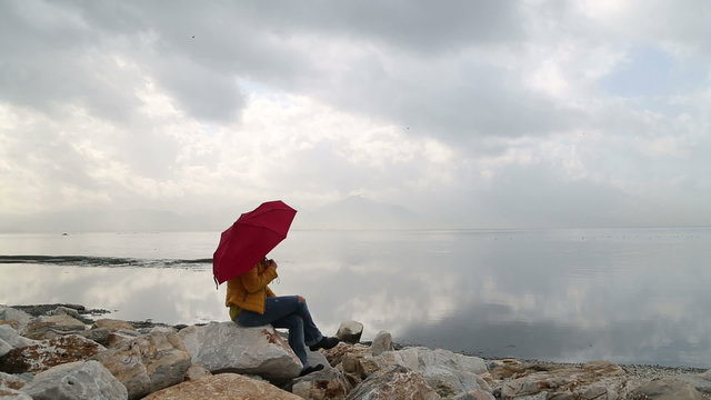 Lonely woman with umbrella,  sitting on the rock at the seashore