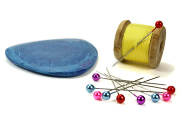 Wooden coil with threads, needle, blue chalk and pins for sewing on a white background