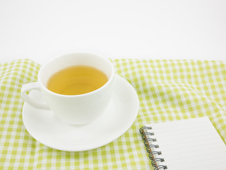 The cup of Japanese green tea and small note book on green cotton fabric.
