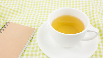 The cup of Japanese green tea and small note book on green cotton fabric.