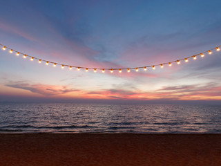 light bulbs on string wire against sunset sky by the beach