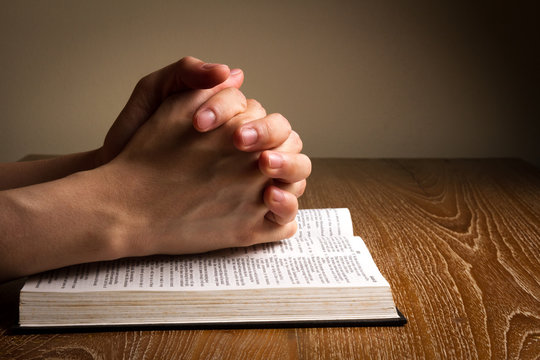 hands praying on bible