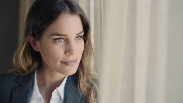Portrait of young business woman in a hotel room by the window looking far away smiling.