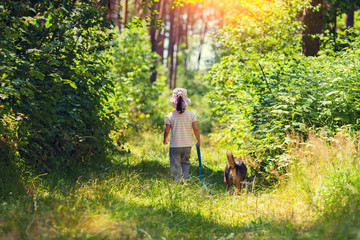 Fototapeta premium Little girl walking with dog in the forest back to camera