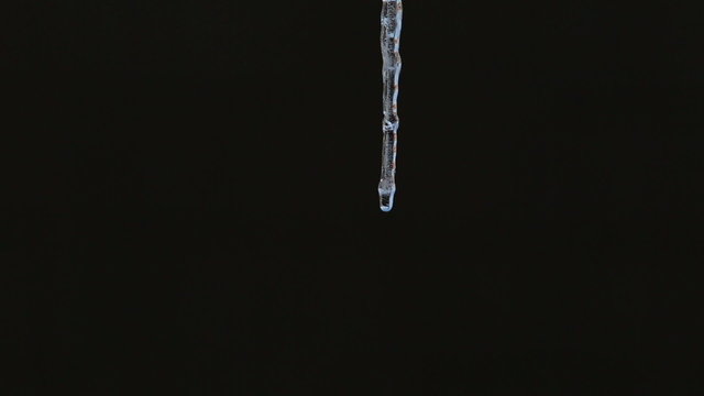 Close up of single clear thick icicle hanging down over isolated black background
