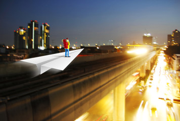 Miniature backpacker on paper airplane in the big city