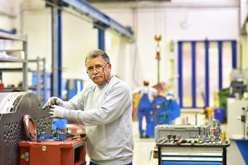 älterer Arbeiter montiert Getriebe in einer Fabrik // portrait industry workers in mechanical...