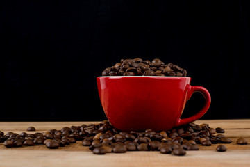 Coffee beans in red cup on wooden table with black background.