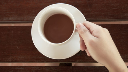 Female hands holding a cup of coffee with foam over wooden table