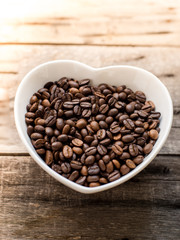 coffee bean in a bowl in the form of heart on a wooden backgroun