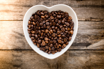 coffee bean in a bowl in the form of heart on a wooden backgroun