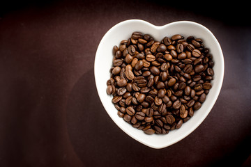 coffee beans in a bowl in the form of heart on a leather backgro