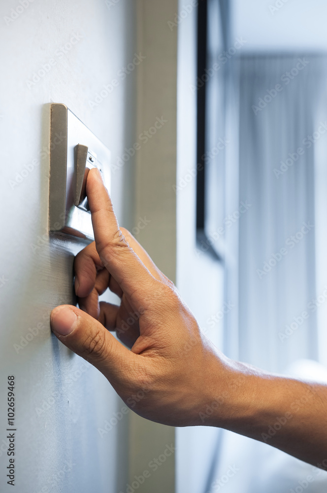 Wall mural hand is turning on a light switch at the livingroom in a house.