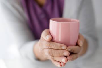 Old woman holding cup of hot coffee drink in her hands