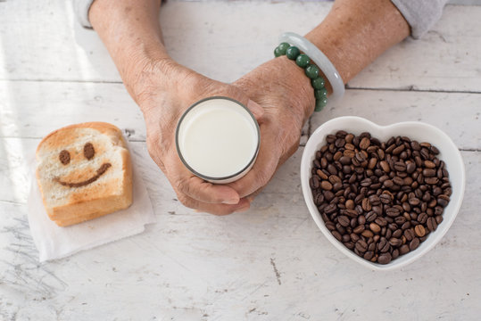 Senior woman's hands holding a glass of milk with coffee beans i