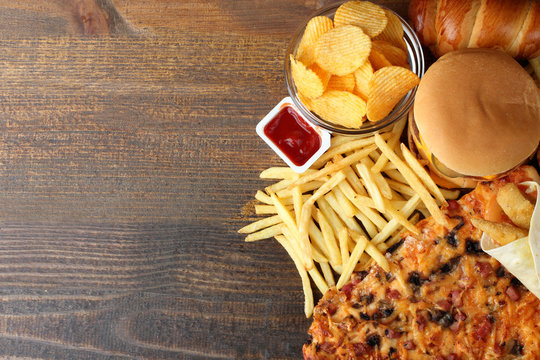 a large piece of delicious pizza and a hamburger with fries on brown wood table